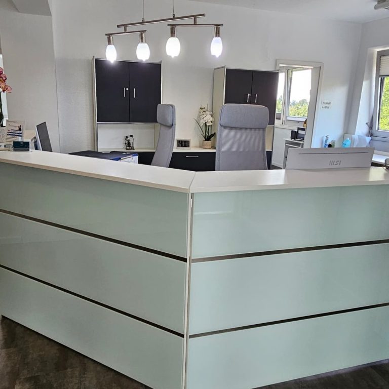 Moderne Empfangstheke in einem hellen, gepflegten Büro mit Stühlen und Pflanzen.